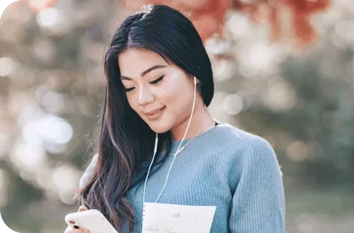A young woman in a blue sweater listening to music on her earphones outdoors