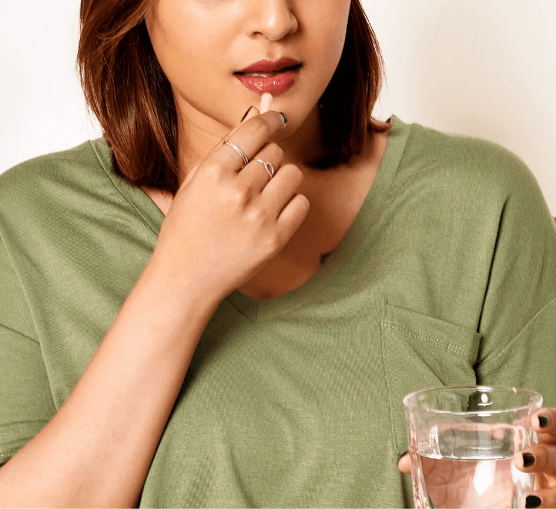 A woman in a green t-shirt taking a pill, a glass of water in her other hand